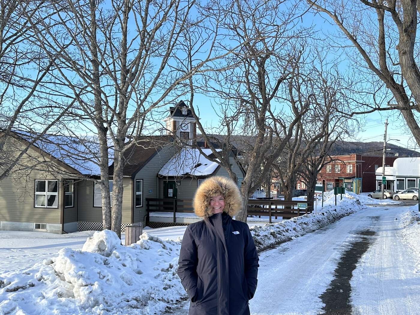 A person in a winter parka on a snow-cleared walkway beside a house on a sunny winter day