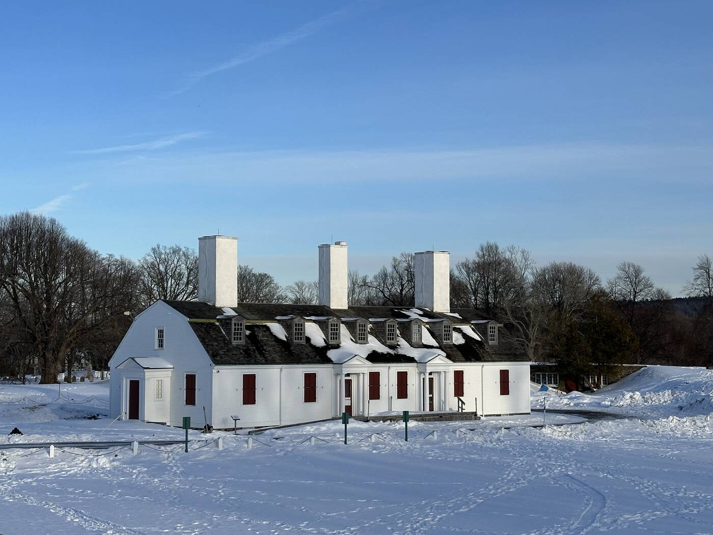 A white historic building with three chimneys surrounded by deep winter snow